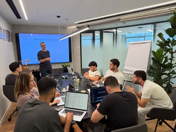 דניאל נחמיה מנחה סדנת AI לצוות בחדר ישיבות, המשתתפים מתרגלים על המחשבים